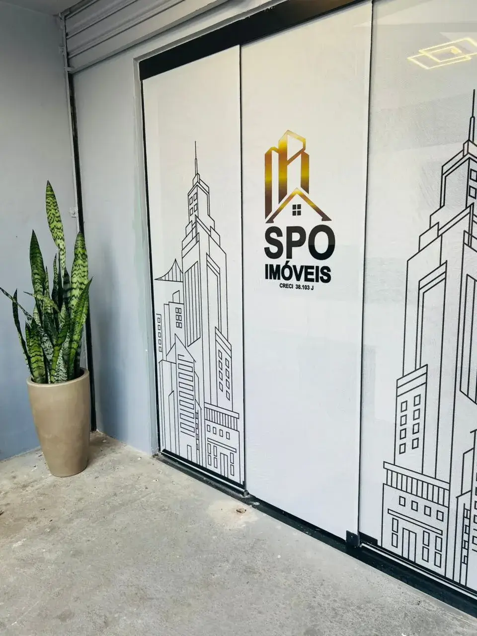 Recepção da SPO Imóveis com porta de vidro adesivada com o logotipo dourado e desenhos de prédios