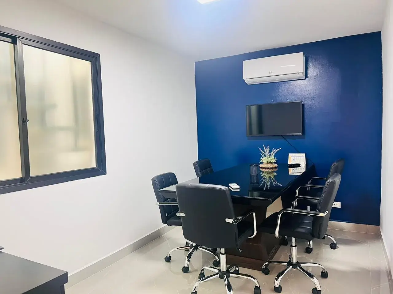 Sala de reunião do escritório da SPO Imóveis, com mesa de vidro, cadeiras pretas e parede azul